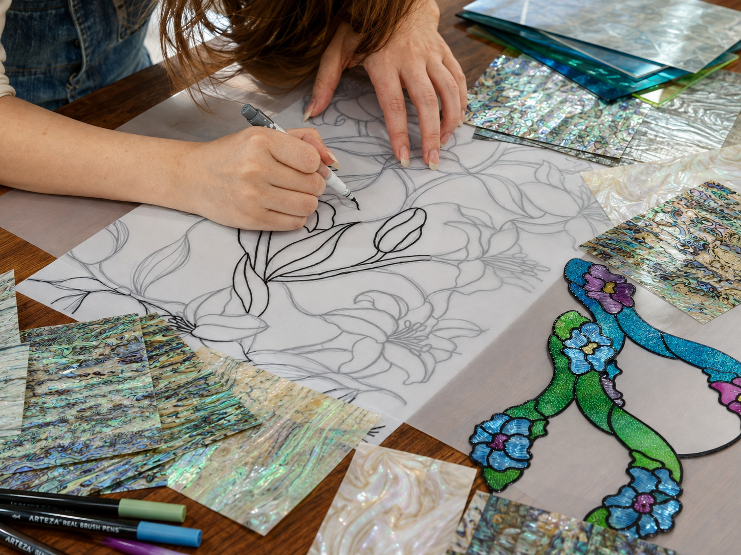 A hand drawing an original floral line pattern beside stained glass film swatches