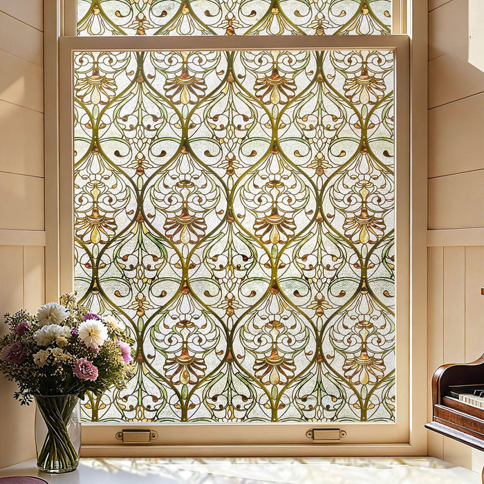 Victorian stained glass window film in amber and olive scrollwork across a sash window, with a vase of flowers and a piano beside it