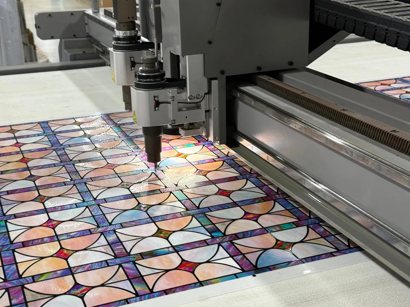 A machine head moving across a freshly printed decorative film sheet on a flatbed table in the factory