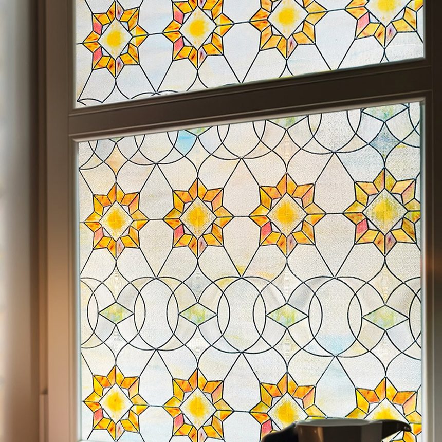 Victorian stained glass window film on a window, amber star medallions lit from behind