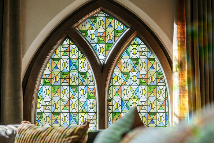 Church and religious stained glass window film in blue, green and amber triangles filling a pointed arch window above a cushioned seat