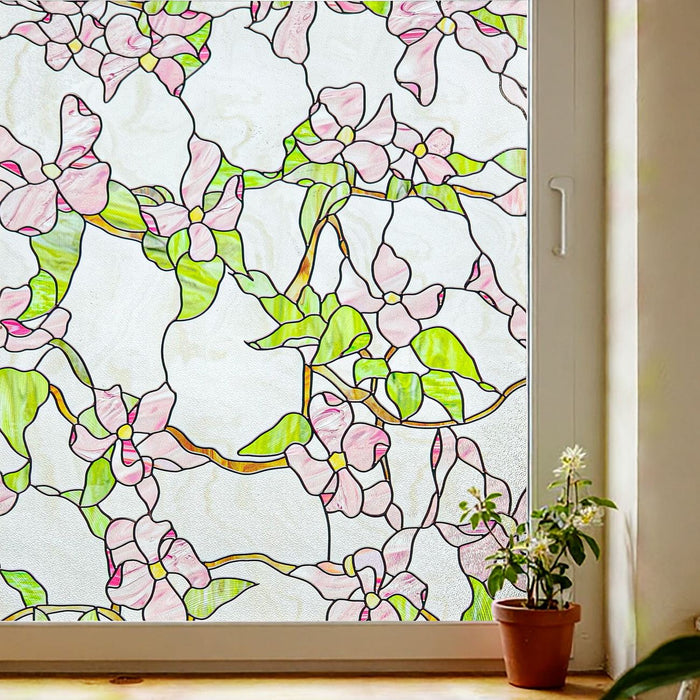 Floral stained glass window film with pink dogwood blossoms and green vines spreading across a window above potted plants