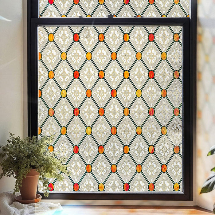 Gothic stained glass window film in a cream diamond lattice studded with amber and red bosses, set in a black window frame beside a potted plant