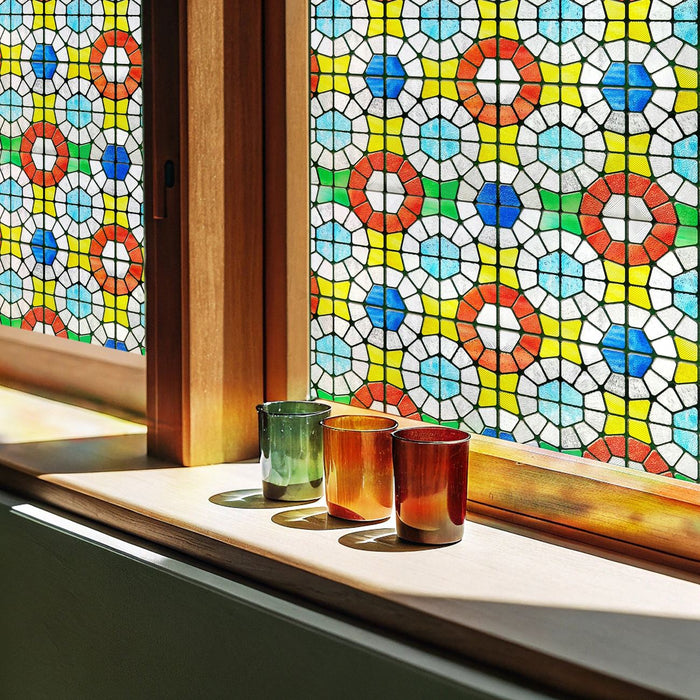 Vintage and antique stained glass window film in a bright mosaic of red, blue and yellow roundels, with three coloured drinking glasses on the sill